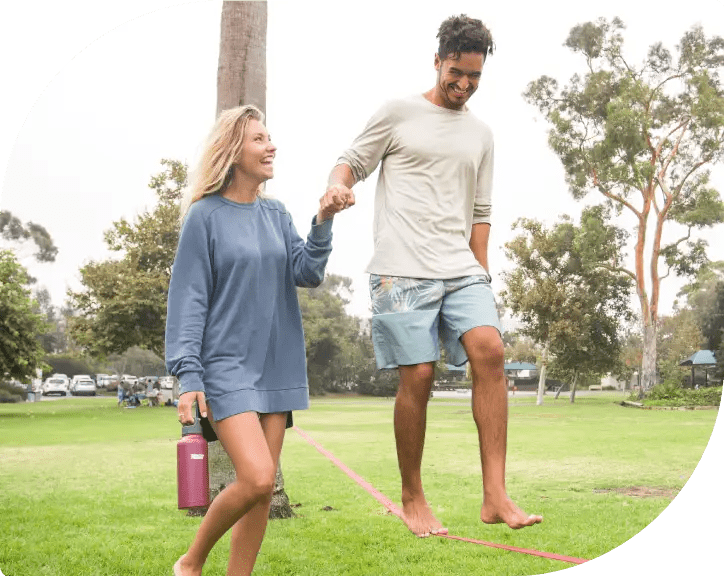 Happy Couple Strolling on Grass, Woman Holding Healthy Human Bottle - Joyful Hydration Together